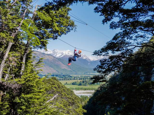 Person ziplining with snow-covered mountain in the back