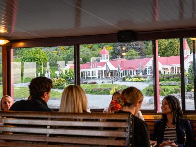 A group of people sitting on the TSS Earnslaw with a view of Walter Peak through the windows