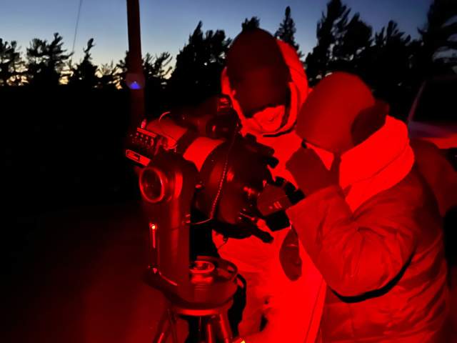 two people peer through a telescope at night