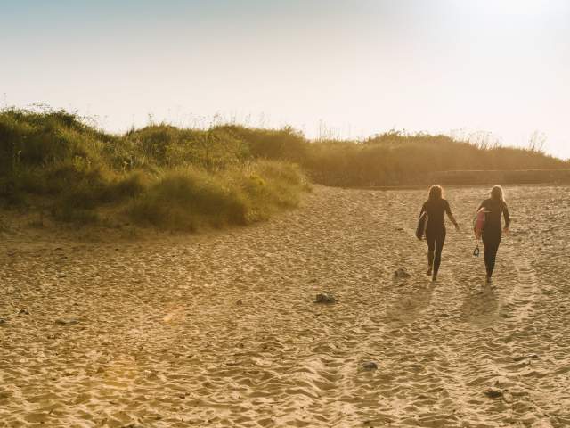 Two ladies walking across the beach with surfboards