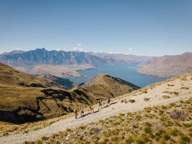 A group of people walking up Ben Lomond peak with mountain ranges and Lake Whakatipu in the background