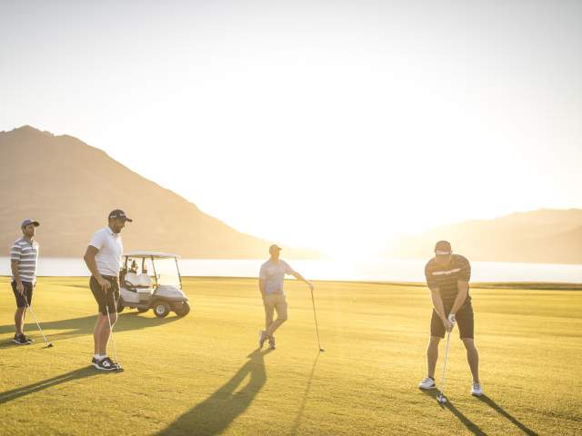 four men playing golf at Jacks Point golf course at sunset with lake and mountains in the background