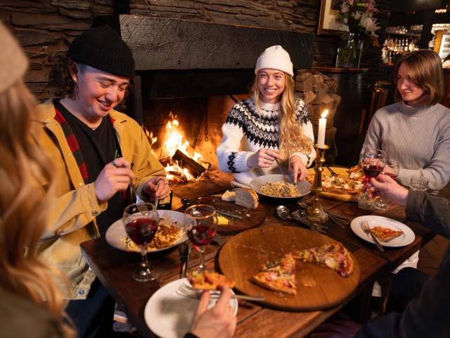 Group of friends eating at a cosy restaurant with fire roaring in the background
