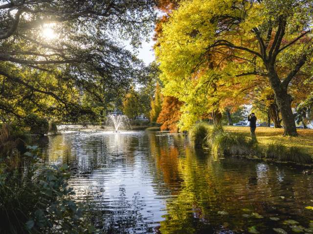 Queenstown Gardens in Autumn, a man takes a photo of a fountain