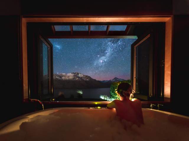 Person in a bath at night with starry view of lake and mountains
