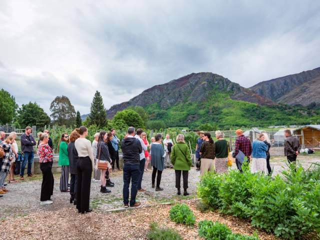 A group of people on a tour around a kitchen garden with mountains and green trees in the background