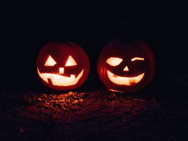 Two jack-o-lanterns glow in candlelight on an October night.