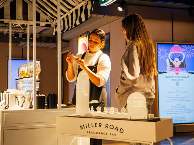 A white stand inside a shop with two girls making perfume