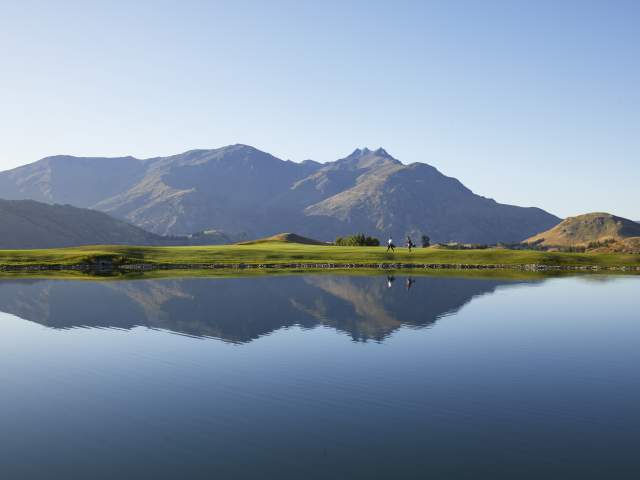 Wide shot of a golf course with lake reflecting mountains