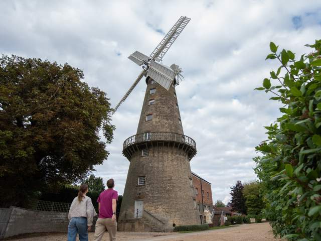 two people walking towards a windmill in the countryside