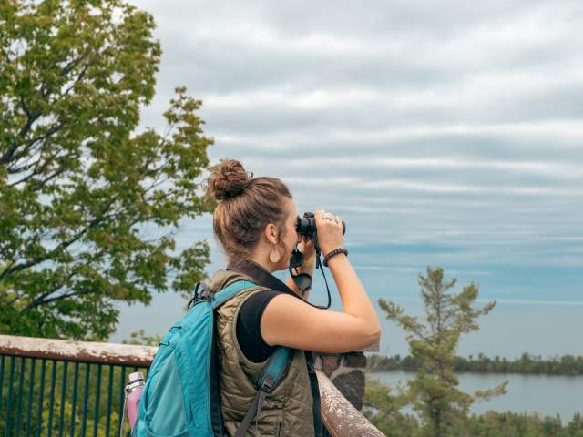 a figure looks through binoculars across a cliffside vita