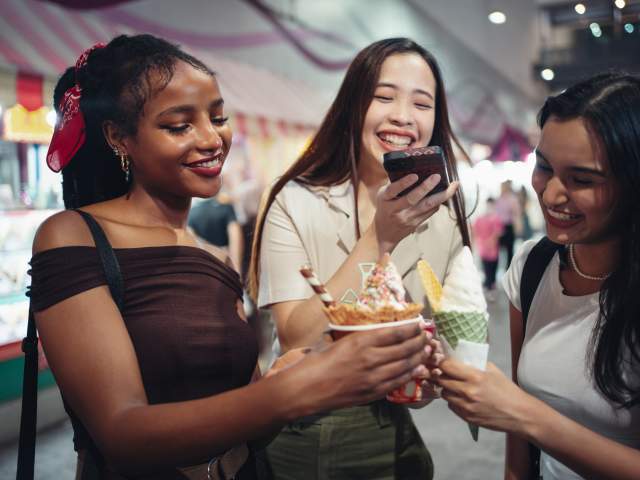 Happy girlfriends capturing a photo of their ice cream in the city at night.