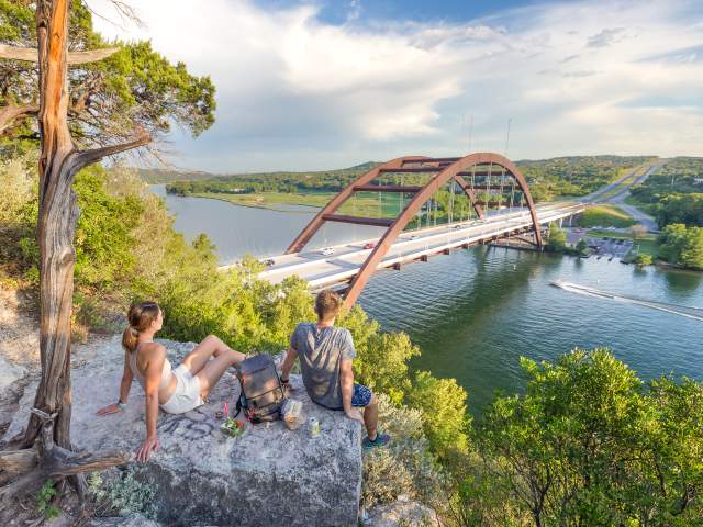 Hikers sitting on a hilltop rock overlooking the Pennybacker Bridge at Lake Austin.