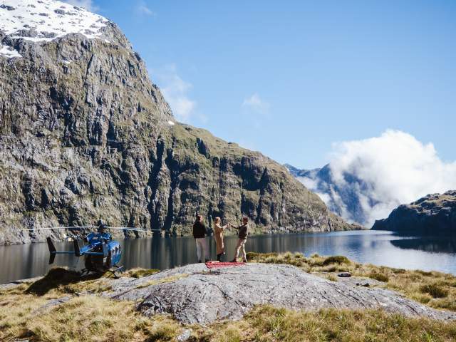 People having a picnic next to a high alpine lake with a helicopter next to them