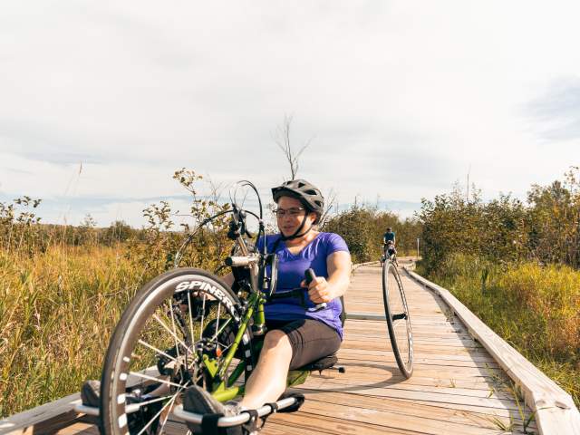 a person uses an adaptive bicycle to cruise a nature boardwalk