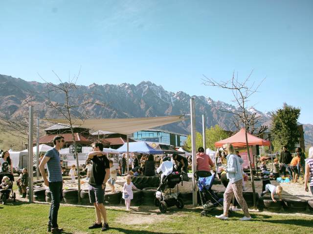 A busy playgorund with a market in the background, set in front of the Remarkables mountain range