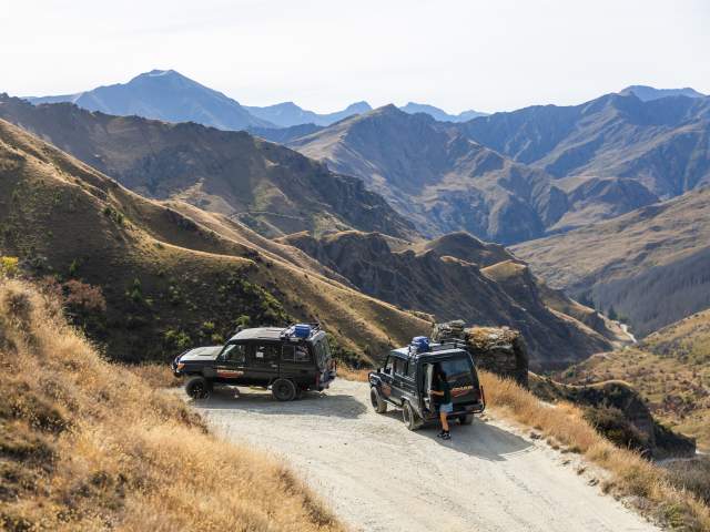 Two 4WD Landcruiser's parked up with a vast viewpoint of a big canyon and rugged mountains surrounding it.
