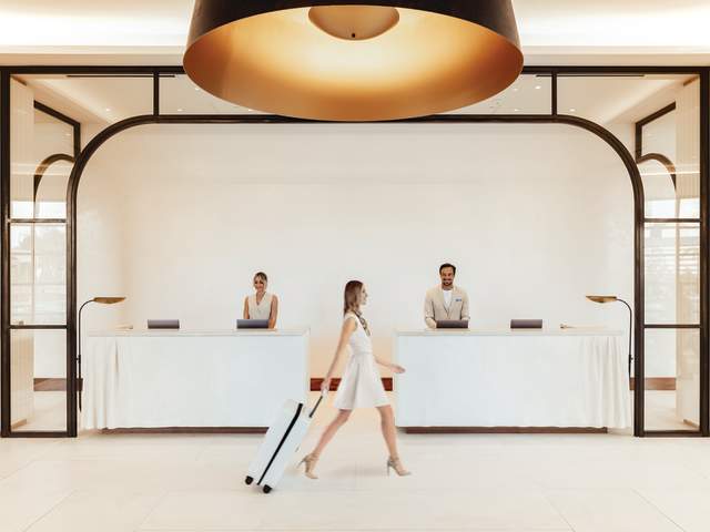 Woman walking fast with luggage past front desk at ette hotel Orlando