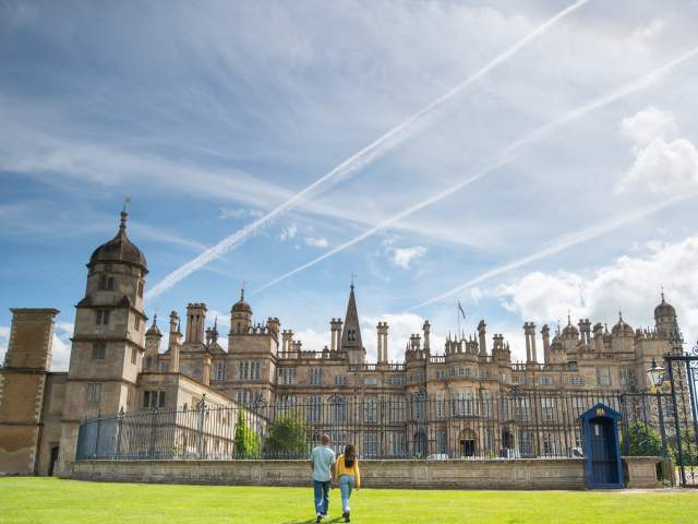 A sunny day exterior of Burghley House near Stamford with two people walking towards the gates