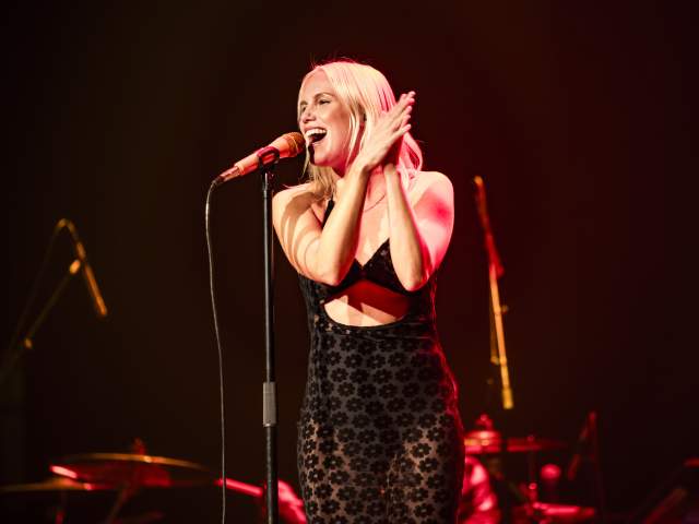 Grace Weber smiling as she sings into a standing microphone and claps