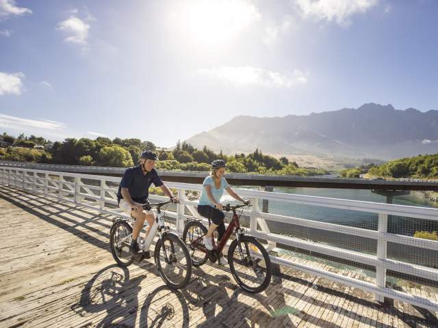 A couple biking the Queenstown Trail with the Remarkables Mountains in the background