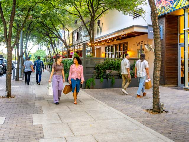 Two women walking down the sidewalk under trees on 2ND Street District with shopping bags