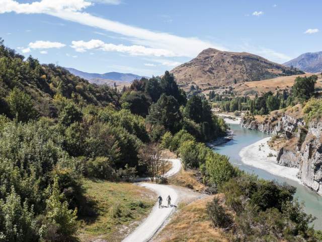 Aerial view of the Shotover Gorge Trail,with two bikers cycling next to a blue river in a Canyon