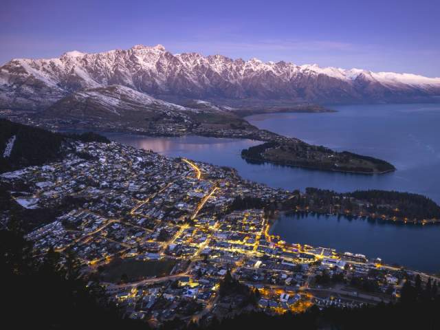 Aerial shot of Queenstown on a winters evening with town street lights glowing and snow capped mountains in the background