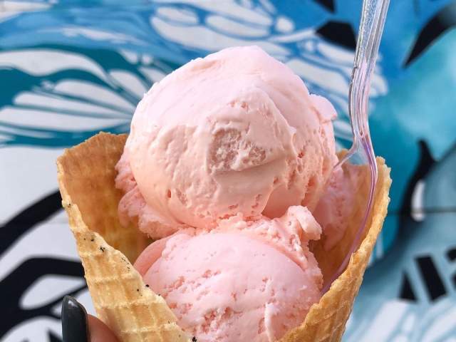 A person holding up a waffle cone with two scoops of pink ice cream