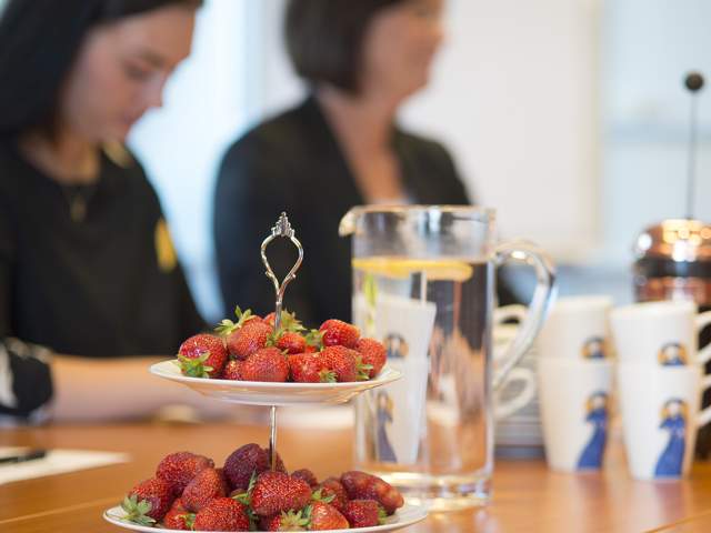 To kvinner sitter i møte med frisk frukt, vann, kaffe og jordbær på bordet