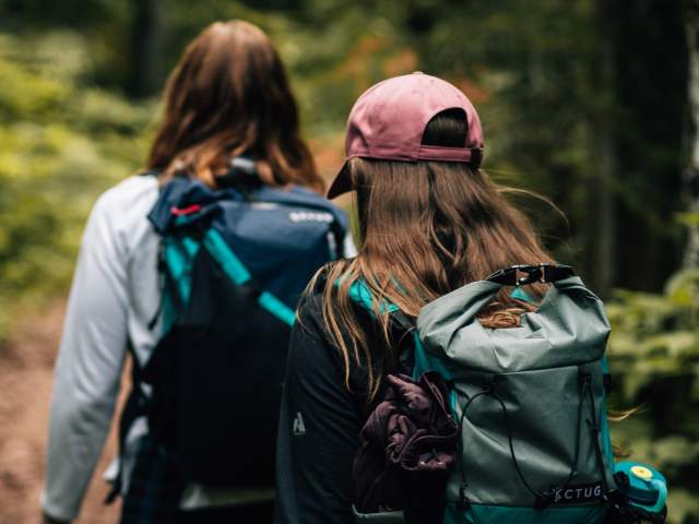 two figures in backpacking gear walk a wooded trail