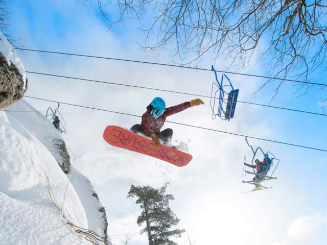 a snowboarder catches air underneath the chairlift
