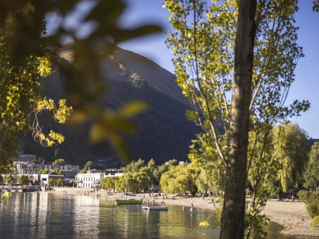 Looking through green trees to big lake, boats, people and buildings