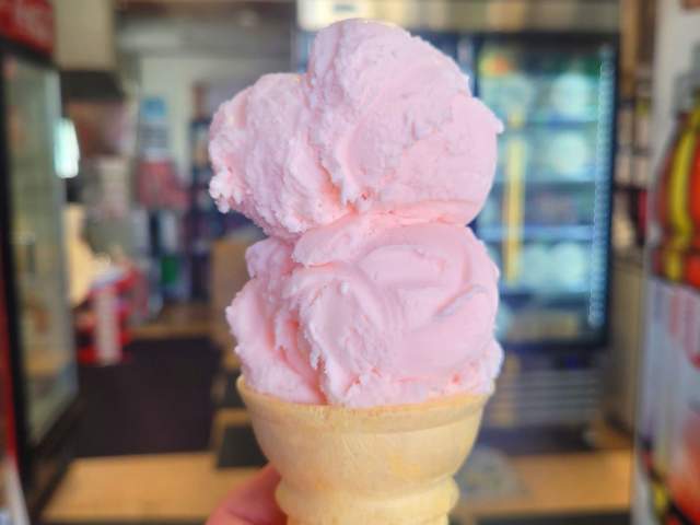 A hand holding a small ice cream cone with two scoops of ice cream