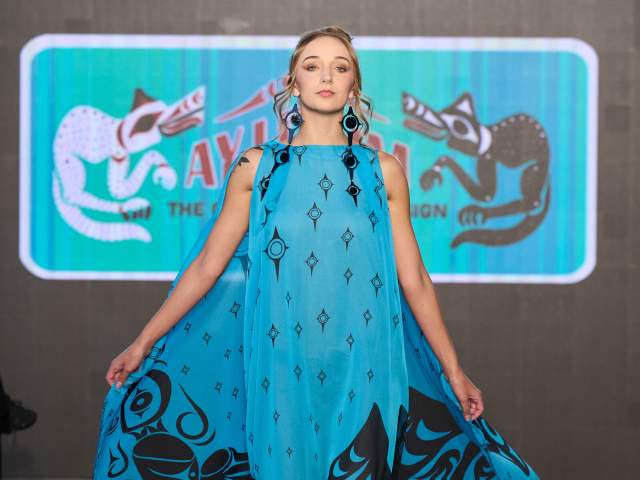 A women in a blue and black dress, Indigenous designs are in black.