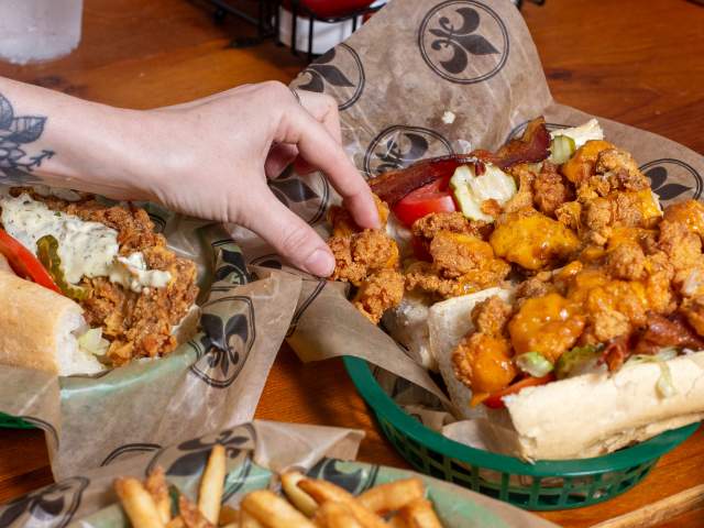 a person reaches for a fried shrimp po-boy and and french fries at Mahony's in New Orleans