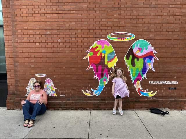 aunt and niece posing with the Silver Lining Creamery angel wings mural.