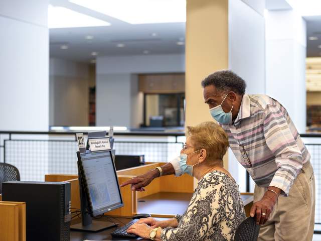 Two adults wearing masks looking at a computer in the Genealogy Center in Fort Wayne, Indiana.