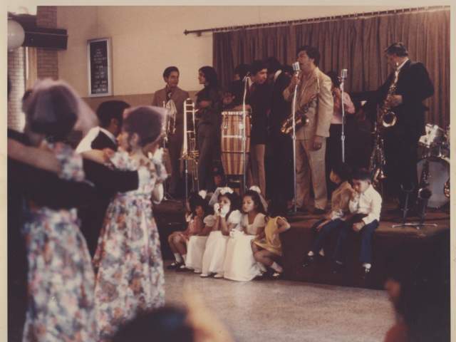 Photo of the Alfonso Ramos Band with saxophone drums bongo drum trombone and trumpet playing at the San Jose Community Center for a wedding party in South Austin around 1970