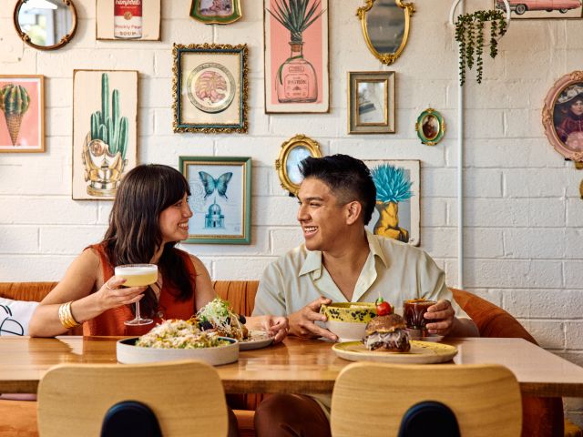 A man and woman sit together at a table in Chilte Restaurant, located in the Grand Ave neighborhood of downtown Phoenix. Plates of food are in front of them, and the wall behind them is covered in framed artwork.