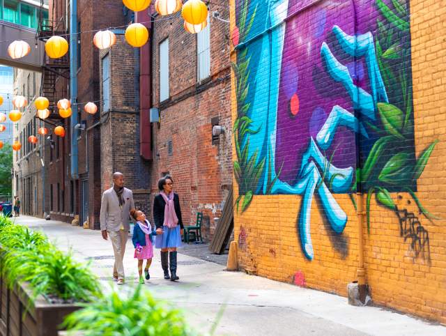 Father, mother, and daughter walking past a mural and the Porch off Calhoun in downtown Fort Wayne, Indiana.