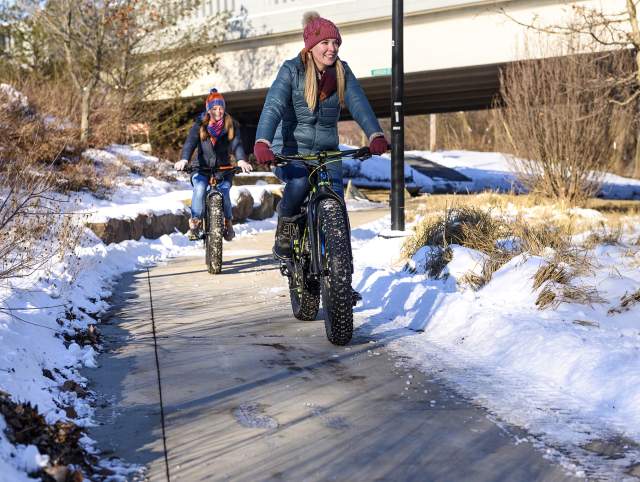 two girls on fat tire bikes on a sidewalk surrounded by snow
