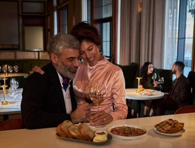 Couple holding each other. Wine in hand and small bites around them.