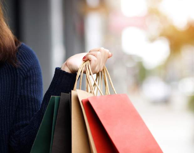 Picture on a persons hand holding shopping bags with a blurry street view in the background.