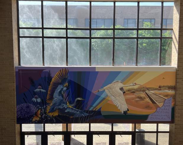 a mural showing birds flying over a marsh and a setting sun in rainbow colors