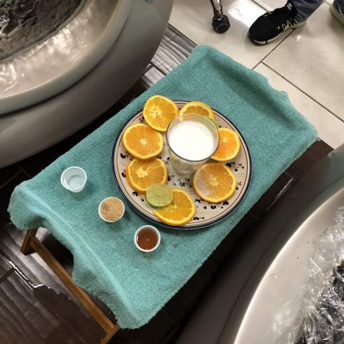 A teal tray holding a plate with orange slices and a glass of milk. Small containers of lotions sit next to the plate.