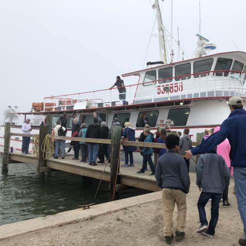 A group of kids and adults waits in line to board a large white boat
