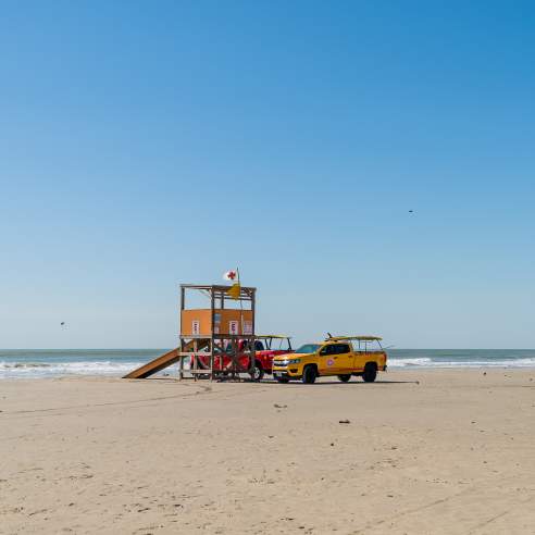 Two trucks sit by a surf rescue tower on the beach