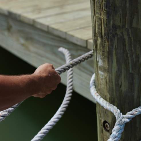 Hands are in the act of tying a white marine rope around a wooden dock pole