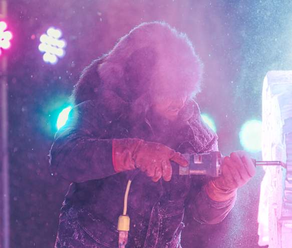 An ice carver using a power tool to carve a sculpture during the Freezefest ice battle